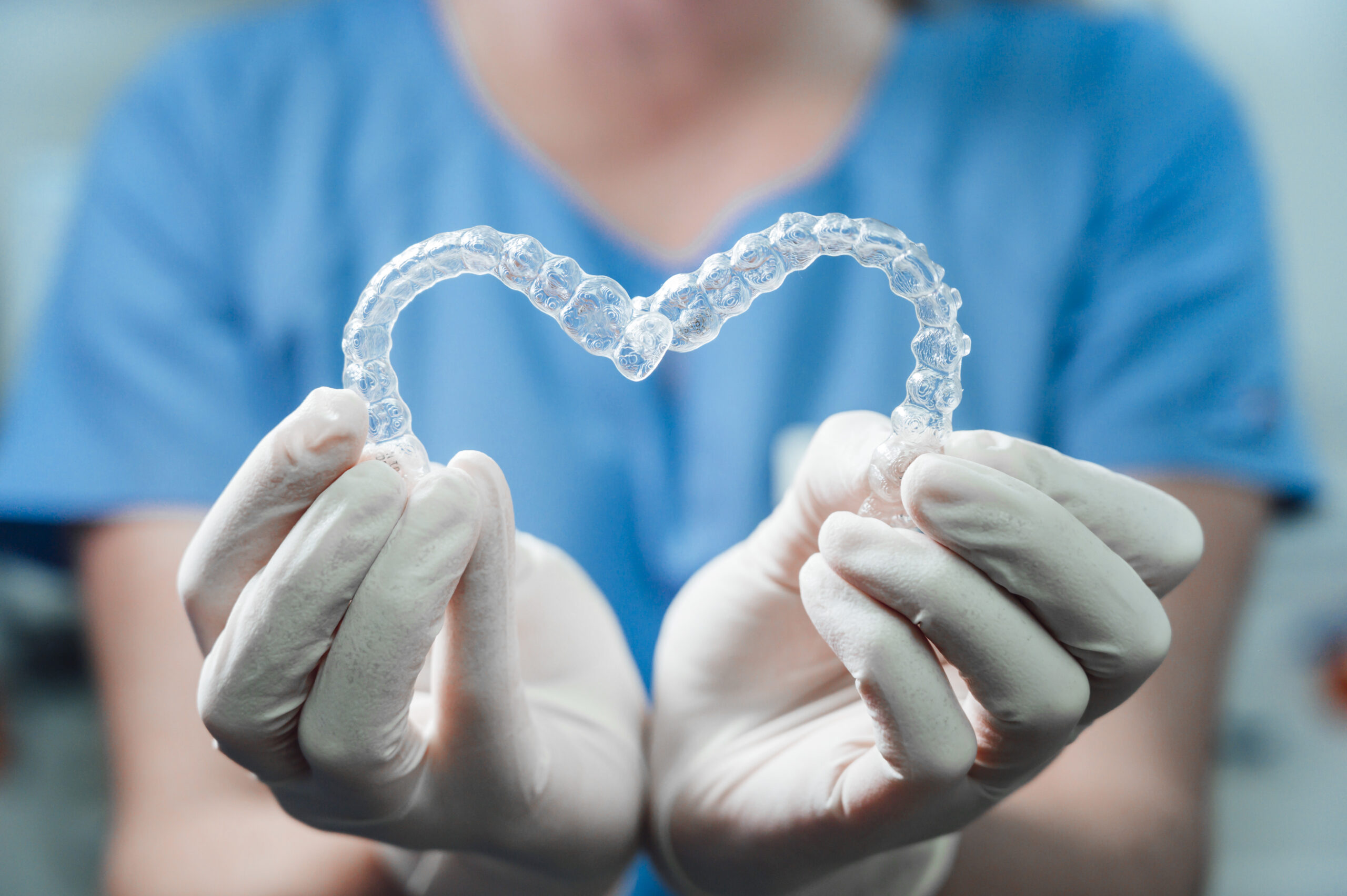 Zahnärztin hält unsichtbare Zahnschienen (Aligner) als Herz geformt in die Kamera
